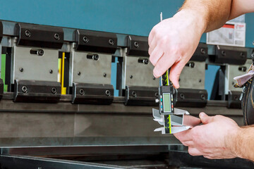 The worker measures the product after bending on a hydraulic press for bending sheet metal.