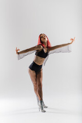 Young beautiful flexible female in black jumpsuit and high heels is posing in a dance studio.