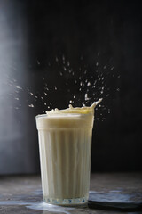 glass of milk with splashes on gray background

