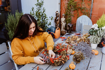 Girl making floral autumn door wreath using colorful rosehip berries, rowan, dry flowers and...