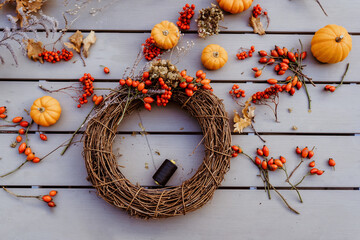 Making floral autumn door wreath from natural materials: colorful rosehip berries, rowan, dry flowers and pumpkins. Fall flower decoration workshop. Top view.