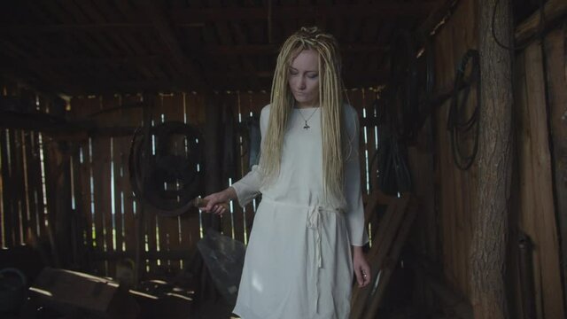 Eerie cruel beautiful drowned woman with pale face and dreadlocks, frightening with bloody sickle in dark rustic shed, raising from dead to revenge for her death, expressing horror and ruthlessness.