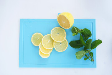 On a white background, a blue board, green mint leaves and a sliced ​​lemon.

