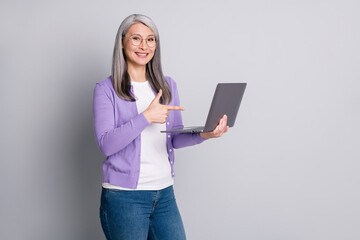 Photo portrait of friendly satisfied smiling old woman holding pointing on laptop with finger isolated on grey color background
