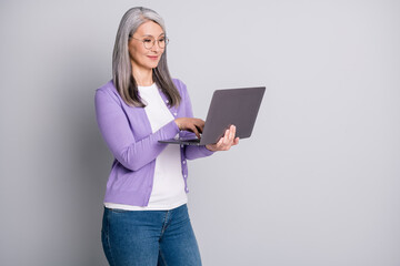 Photo portrait of smiling confident senior businesswoman wearing eyeglasses working with modern laptop reading searching in internet isolated on grey color background