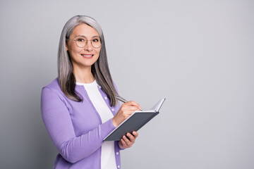 Portrait photo of elder smiling businesswoman writing down notes plans in organizer wearing...