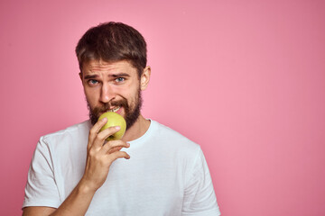 Cute man with an apple on a pink background gestures with his hands cropped white T-shirt Copy Space