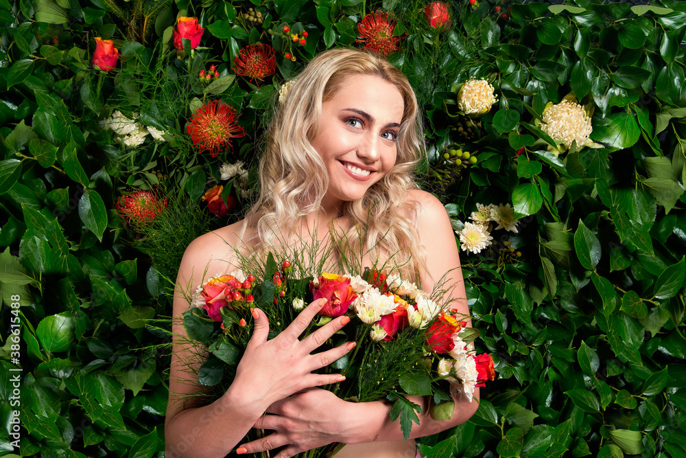 Wall mural A beautiful young blonde lady standing in front of a wall of flowers holding a bouquet