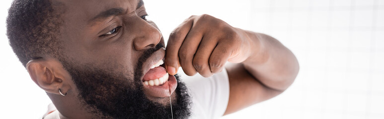 Obraz premium panoramic view of afro-american man using dental floss
