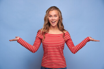 Portrait of a surprised girl in striped clothes holding a copy of an empty space on a blue...