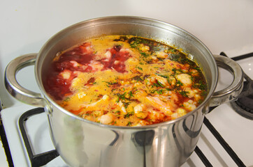 Metal saucepan with boiling vegetable soup on a gas stove. Cooking for a large family, traditional first course.