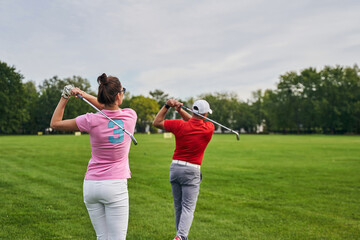 Two athletes practicing golf swings on the driving range