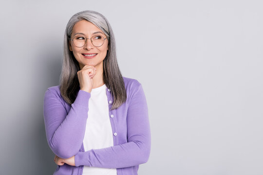 Portrait photo of smart elder intelligent business woman wearing eyeglasses looking at side thinking about idea touching face smiling isolated on grey color background
