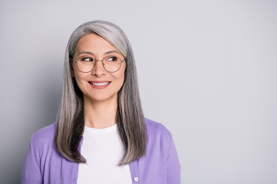 Portrait photo of satisfied smiling senior businesswoman wearing eyeglasses and purple cardigan dreaming planning isolated on grey color background