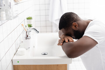 tired afro-american man leaning head on sink