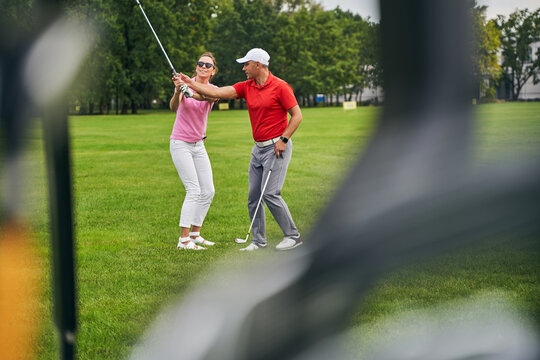 Smiling female beginner taking a golf lesson from a professional - Powered by Adobe