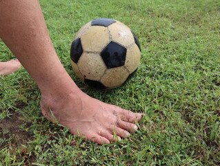 Bared feet of a kid beside A black and white striped soccer ball on the lawn