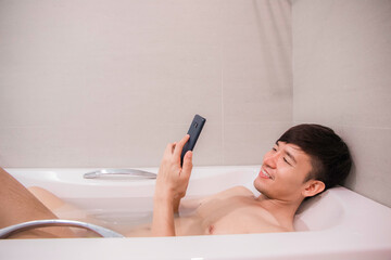 Obraz na płótnie Canvas Asian guy check smartphone in bathtub-happy smile