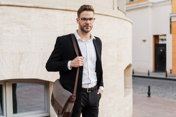 Handsome unshaven businessman posing with bag on city street