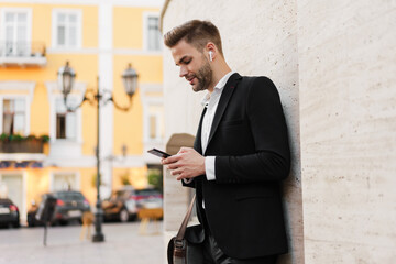 Handsome serious businessman using wireless earphones and mobile phone