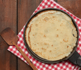 baked round big pancake in a black frying pan