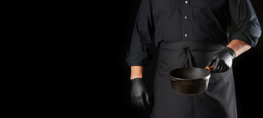 cook in black uniform and latex gloves holds an empty round vintage black cast iron pan