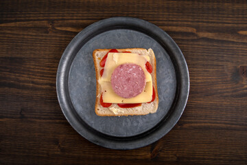 Sandwich on a metal plate. Healthy and unhealthy food concept. Dark wooden background