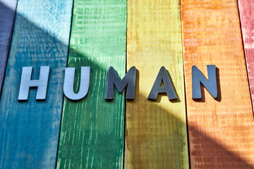 Old wooden boards in the colors of the LGBT flag, with an inscription in iron letters on them human