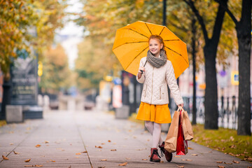 girl with a bright jelly umbrella and with shopping guide walks along the autumn city boulevard...