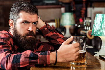 Single bearded man at the bar counter. Alcohol addiction. Bearded man holds glass of beer.