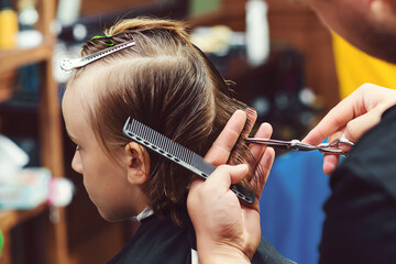 Hairdresser with scissors. Barber shop. Childhood. New hairstyle for young boy.