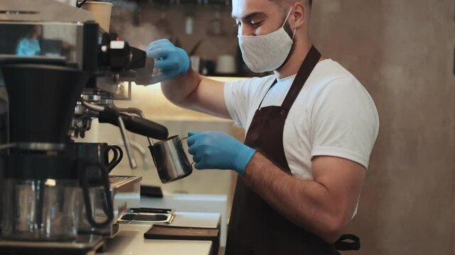 A side view of handsome young guy barista is making coffee behind the counter during quarantine indoors