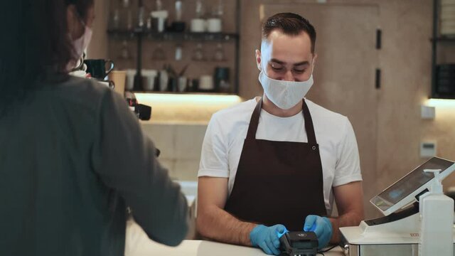 A customer is paying by smartphone card while buying coffee during quarantine indoors