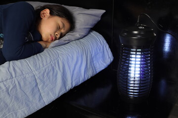 a pretty young girl sleeping near the insects mosquito electric killer blue light lamp is put on the wooden bed table in the dark bedroom  for better sleeping ambient safty condition at night