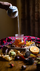 Pouring hot water from teapot to glass of Glass cup with hot infused tea with orange and cloves closeup, fall warming beverage, cozy and hygge autumn home concept