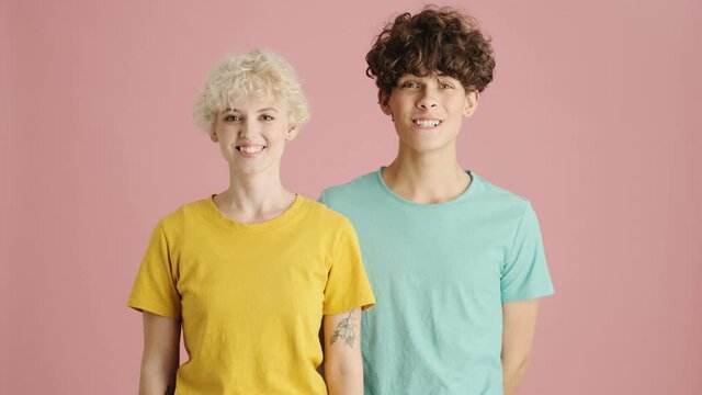 Happy young sister and brother are smiling while looking to the camera standing isolated over pink background