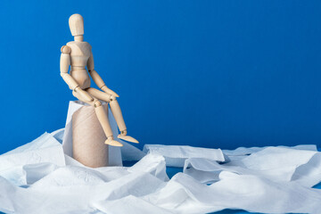 The little wooden man sits on empty toilet paper. Bowel problems, incontinence and diarrhea concept.