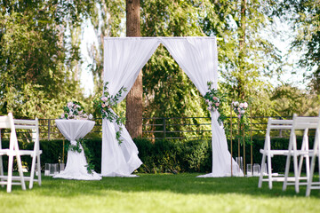 A wedding arch decorated with natural flowers stands on a green lawn in the forest. Everything is...