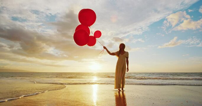 Beautiful happy young woman holding red balloons on the beach at sunset, happiness and wellness concept