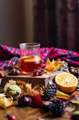 Fototapeta na wymiar Glass cup with hot infused tea with orange and cloves closeup, fall warming beverage, cozy and hygge autumn home concept