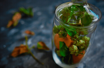 Glass vase stands on the table, there are tangerines and leaves around, the view is close by.