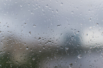 Small wet raindrops on window glass. Damp rainy sad weather. Blurry outlines of city outside the window