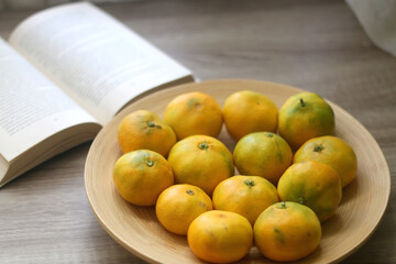 Bowl of tangerines and open book on a table. Selective focus.