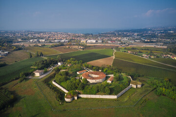 Fototapeta premium Forte Ardietti rises between the territories of Peschiera del Garda and Ponti sul Mincio, Italy. Aerial view of the fortress surrounded by vineyards. Fortified Austrian fort top view on the hill.