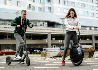 Young man riding electric kick scooter and young woman in casual wear riding unicycle on city street © bortnikau