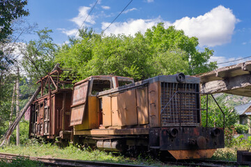 Old rusty diesel locomotive with broken wooden cargo wagon on railway