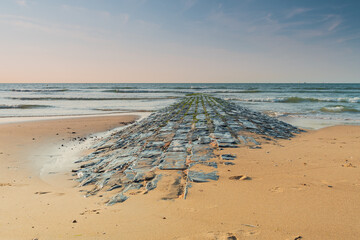 The stone breakwater extends to the sea while the waves come to the sand and the tide drains away from the shore.