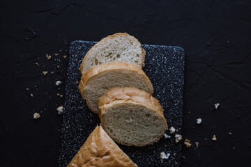 Sliced baguette on cutting board. Dark background. Top view.