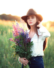 Girl with lupines in shirt and hat at sunset