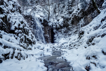 Winter landscape of a waterfall in the mountains and a mountain river running among the stones. Long exposure.